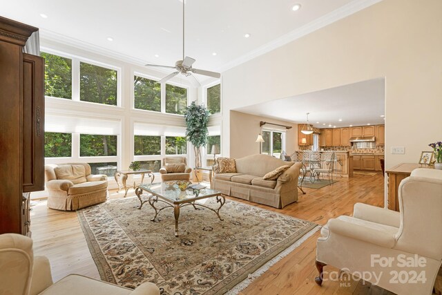 living room with a high ceiling, light hardwood / wood-style flooring, ornamental molding, and ceiling fan