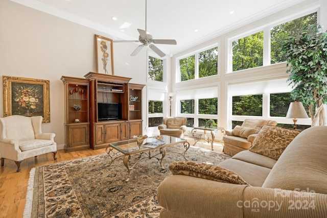 living room with a towering ceiling, crown molding, light wood-type flooring, and ceiling fan