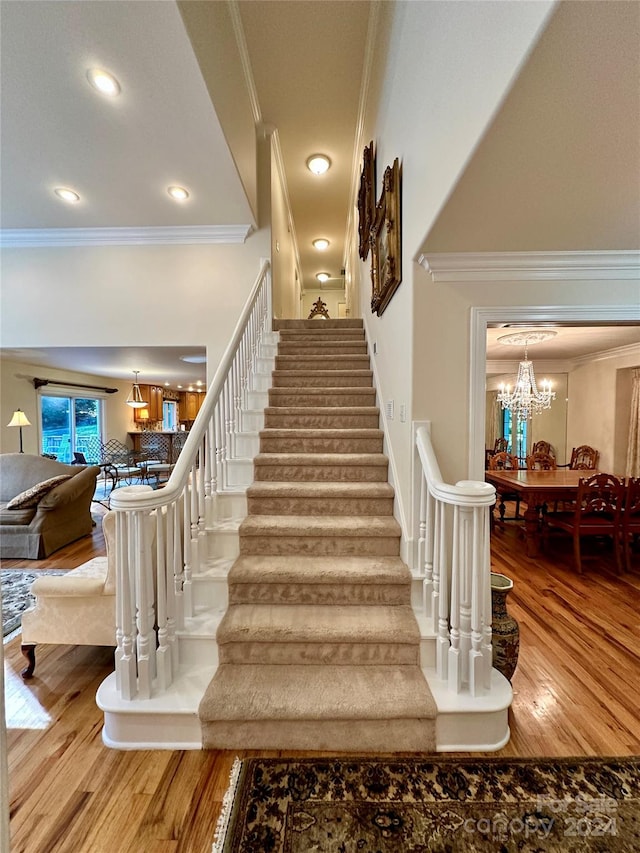 stairs with hardwood / wood-style flooring, crown molding, and an inviting chandelier