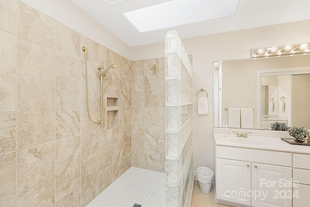 bathroom with a skylight, tile patterned flooring, vanity, and a tile shower