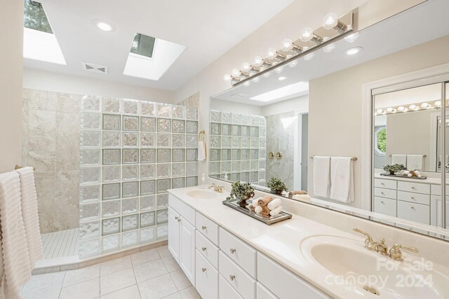 bathroom with tiled shower, tile patterned flooring, dual bowl vanity, and a skylight