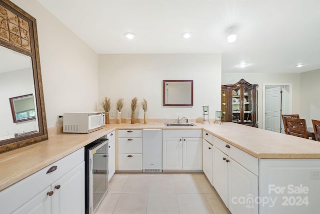 kitchen with light tile patterned flooring, white cabinetry, beverage cooler, sink, and kitchen peninsula