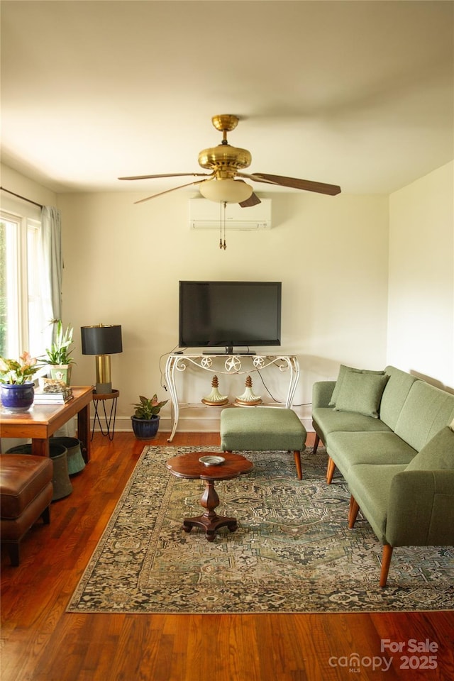 living room with a ceiling fan, a wall mounted air conditioner, baseboards, and wood finished floors