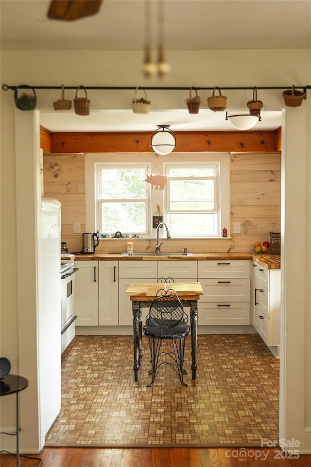 kitchen featuring a sink, butcher block countertops, white cabinets, and electric range oven