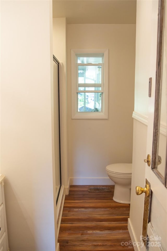 bathroom featuring visible vents, toilet, a shower with door, wood finished floors, and vanity