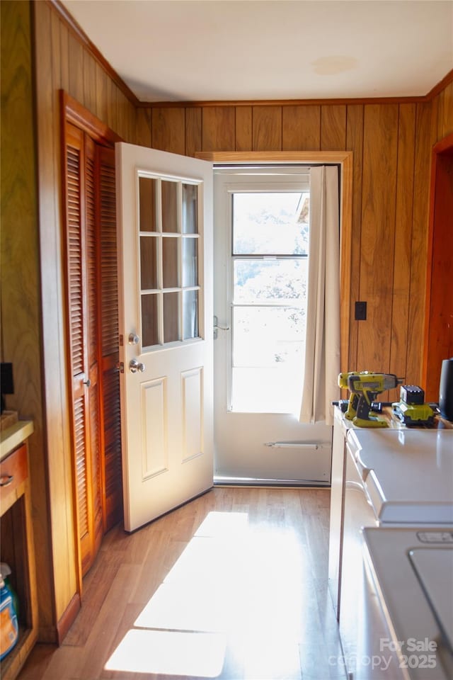 doorway featuring ornamental molding, light wood-type flooring, and wood walls