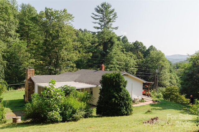 view of home's exterior with a shingled roof, a lawn, a chimney, and a forest view