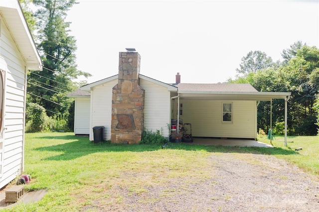 view of side of home featuring a yard, an attached carport, a chimney, and driveway