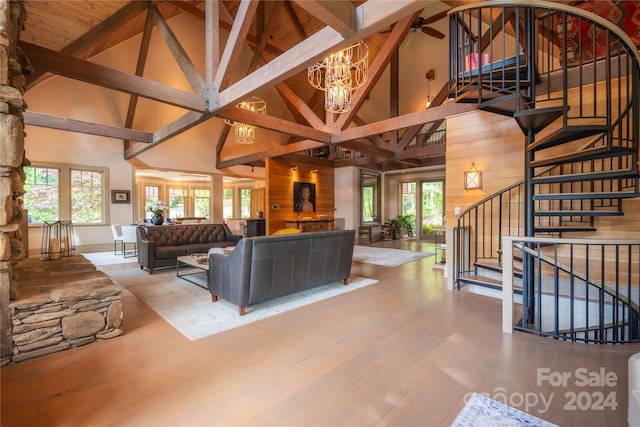 living room with a notable chandelier, beamed ceiling, wood walls, and high vaulted ceiling