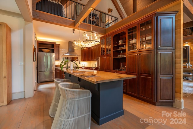 kitchen with high quality fridge, ventilation hood, a center island with sink, and light wood-type flooring