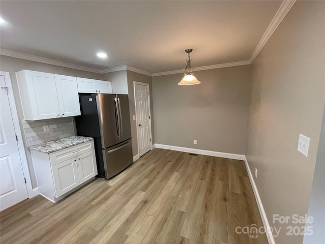 kitchen featuring white cabinetry, ornamental molding, stainless steel fridge, light stone countertops, and light hardwood / wood-style floors