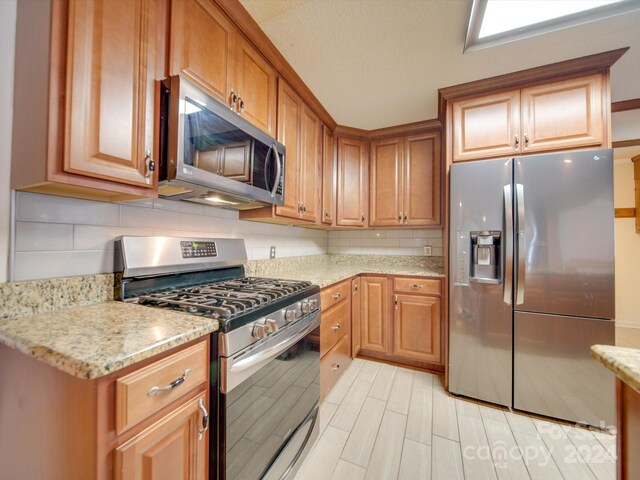 kitchen with decorative backsplash, stainless steel appliances, and light stone counters