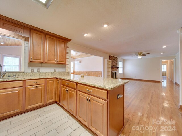 kitchen with kitchen peninsula, ceiling fan, light stone countertops, a fireplace, and light hardwood / wood-style floors