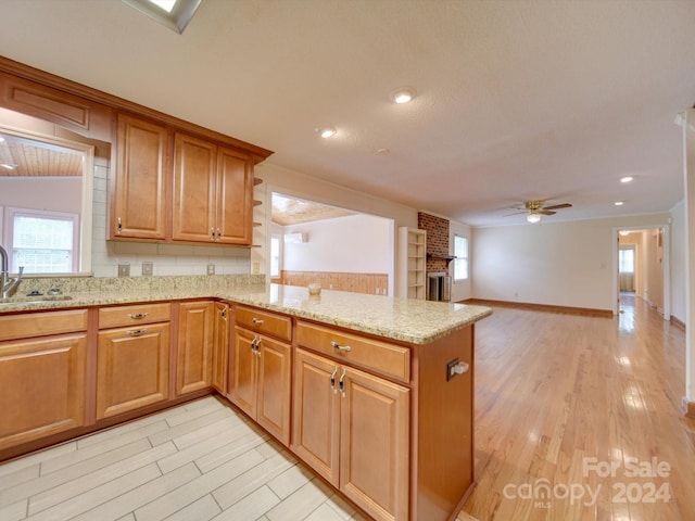 kitchen with a fireplace, ceiling fan, kitchen peninsula, light stone countertops, and light wood-type flooring