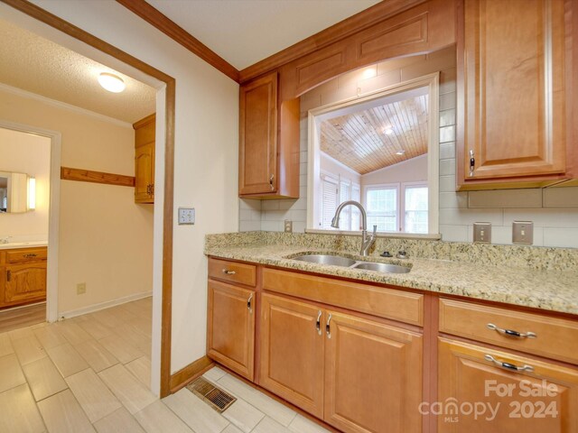 kitchen with lofted ceiling, decorative backsplash, light stone counters, crown molding, and sink