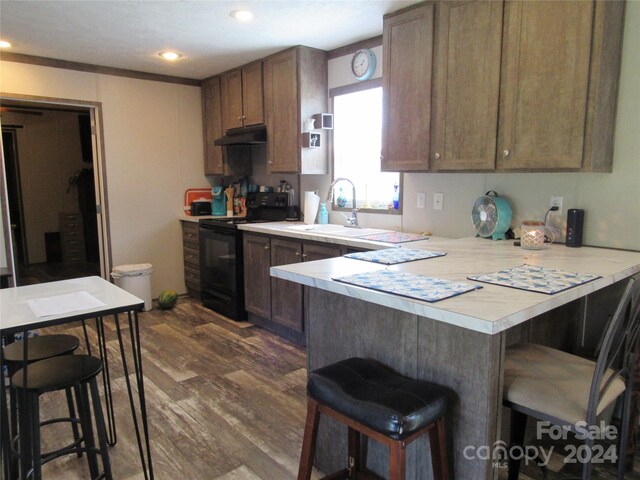 kitchen with dark hardwood / wood-style floors, kitchen peninsula, black / electric stove, and a breakfast bar