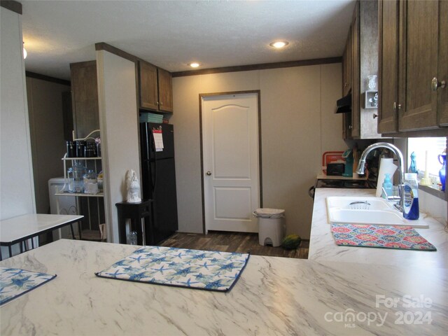 kitchen with dark wood-type flooring, crown molding, black fridge, and sink