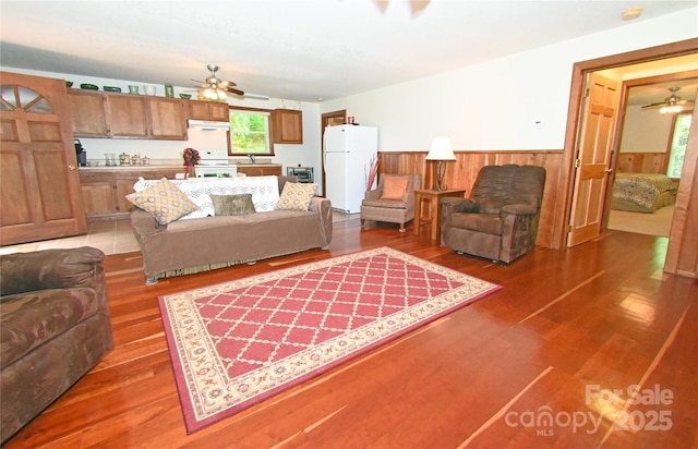 living room featuring wood-type flooring, sink, ceiling fan, and wood walls