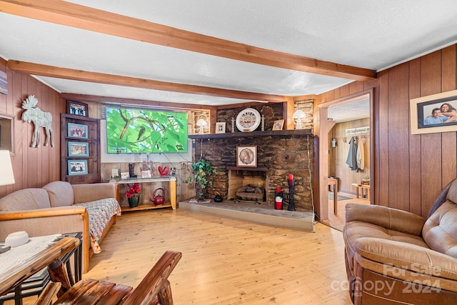 living room featuring beam ceiling, a stone fireplace, light hardwood / wood-style floors, and wooden walls