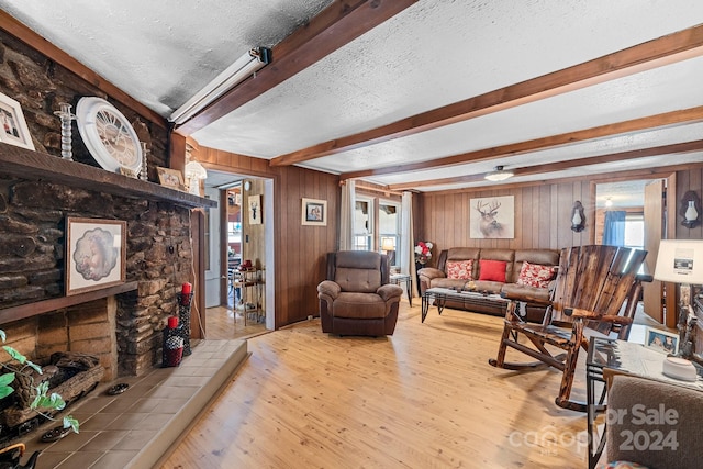 living room featuring light wood-type flooring, beamed ceiling, a textured ceiling, and wooden walls