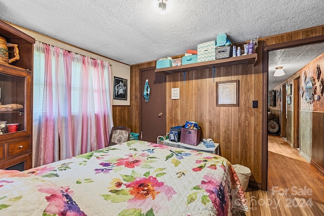 bedroom with wood walls, a textured ceiling, and hardwood / wood-style floors