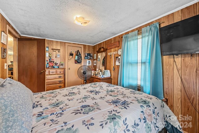 bedroom with a textured ceiling, wood walls, and ornamental molding