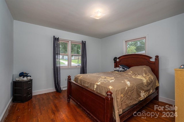 bedroom with multiple windows, dark wood-type flooring, and baseboard heating