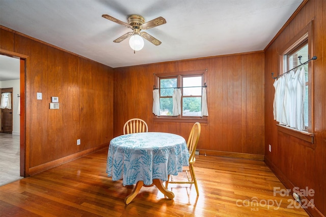 dining space with ceiling fan, wooden walls, and light hardwood / wood-style floors