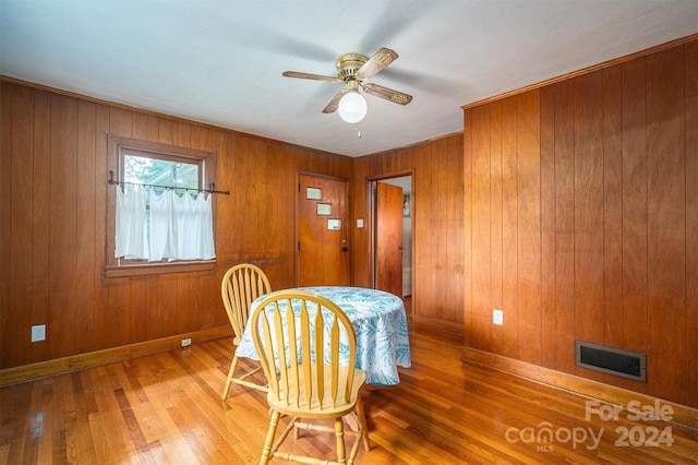 dining space with ceiling fan, wood-type flooring, and wooden walls