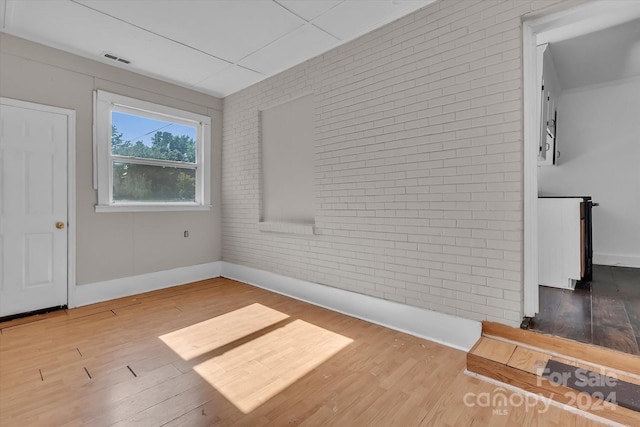 unfurnished room featuring wood-type flooring and brick wall