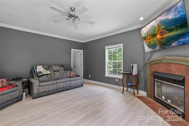 living room with light hardwood / wood-style flooring, a textured ceiling, ceiling fan, a tile fireplace, and ornamental molding