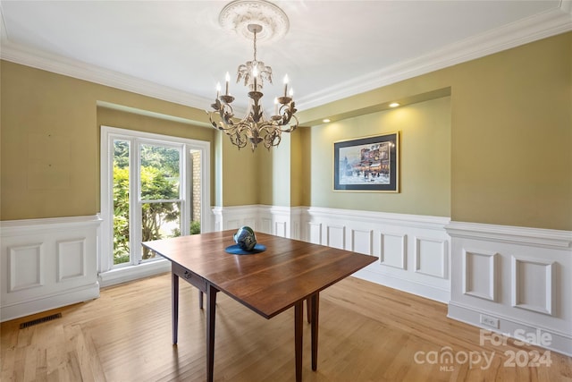 dining space featuring a notable chandelier, crown molding, light wood-type flooring, wainscoting, and visible vents