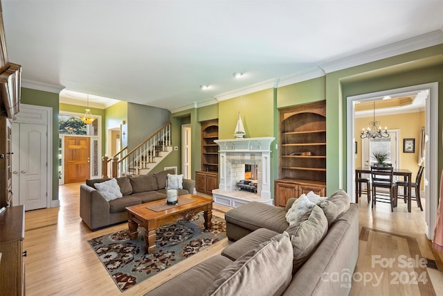 living room with light wood-type flooring, ornamental molding, a chandelier, and a tile fireplace