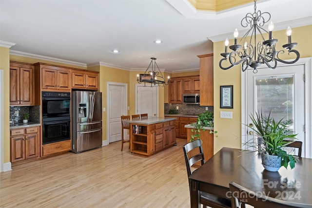 kitchen with an inviting chandelier, a kitchen island, light wood-style flooring, appliances with stainless steel finishes, and brown cabinets
