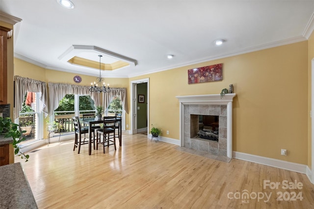 dining room with ornamental molding, a chandelier, light hardwood / wood-style flooring, a tile fireplace, and a tray ceiling