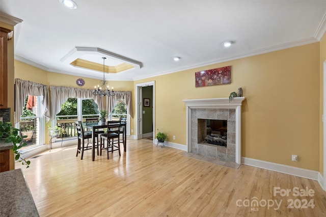dining room with a tile fireplace, crown molding, wood finished floors, a tray ceiling, and a notable chandelier