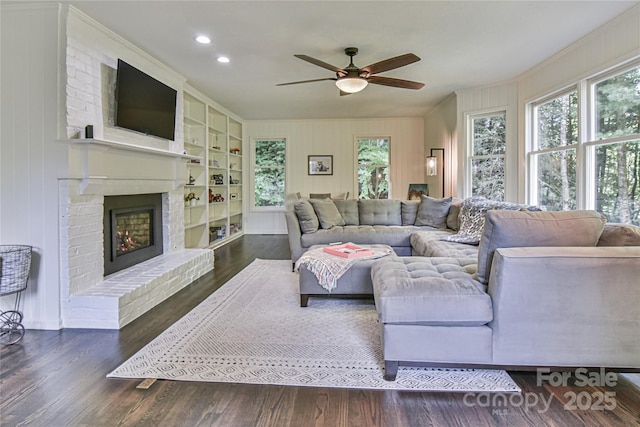 living room featuring dark hardwood / wood-style flooring, ceiling fan, built in features, and a fireplace