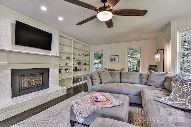 living room with a brick fireplace, dark wood-type flooring, a wealth of natural light, and ceiling fan