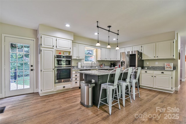 kitchen featuring a breakfast bar area, appliances with stainless steel finishes, a center island, light stone countertops, and white cabinets