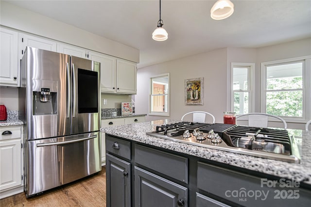 kitchen with light hardwood / wood-style flooring, white cabinetry, stainless steel appliances, light stone countertops, and decorative light fixtures