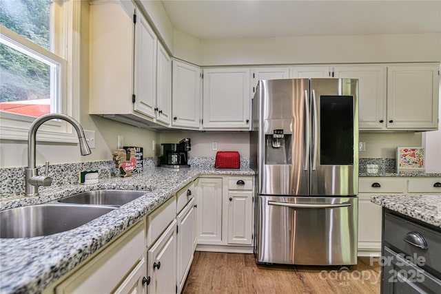 kitchen with sink, stainless steel fridge with ice dispenser, light stone countertops, light hardwood / wood-style floors, and white cabinets