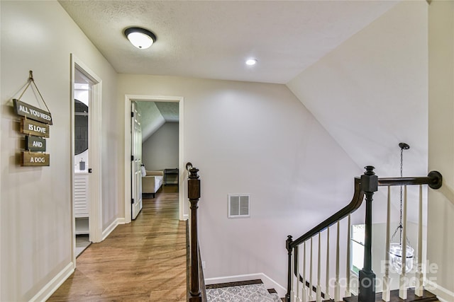 hallway with hardwood / wood-style flooring, vaulted ceiling, and a textured ceiling