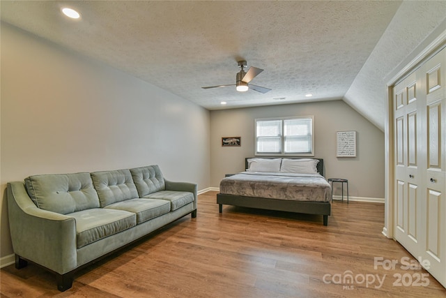 bedroom with ceiling fan, wood-type flooring, vaulted ceiling, and a textured ceiling