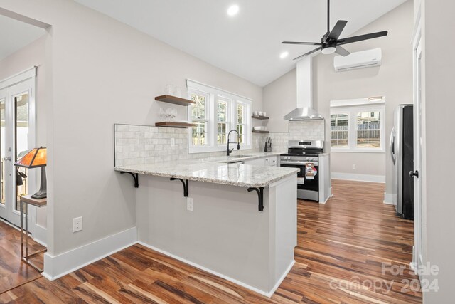 kitchen with a wall mounted air conditioner, a breakfast bar, lofted ceiling, backsplash, and appliances with stainless steel finishes