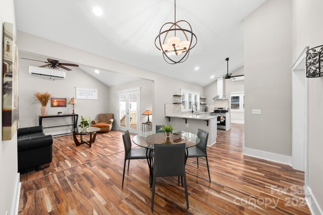 dining area with ceiling fan with notable chandelier, vaulted ceiling, a wall unit AC, dark wood-type flooring, and sink