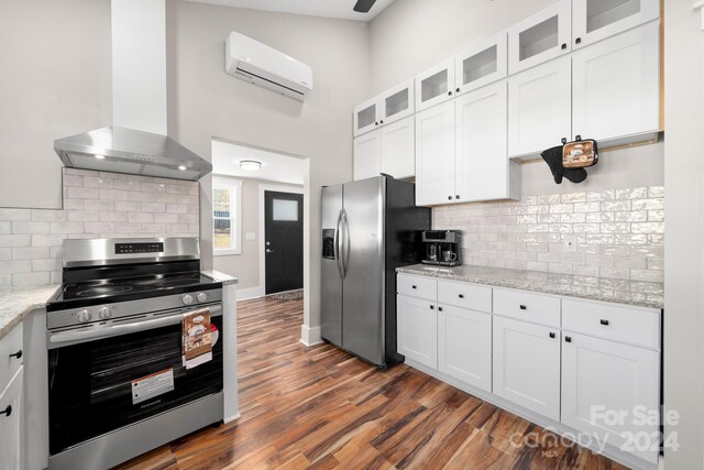 kitchen with appliances with stainless steel finishes, light stone counters, wall chimney exhaust hood, a wall unit AC, and white cabinetry