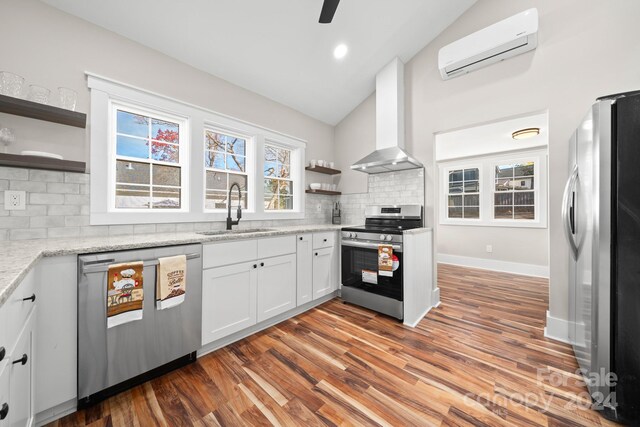 kitchen with appliances with stainless steel finishes, wall chimney exhaust hood, vaulted ceiling, sink, and white cabinets