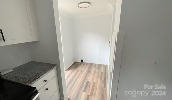 kitchen featuring hardwood / wood-style floors, stone countertops, white cabinetry, and black / electric stove