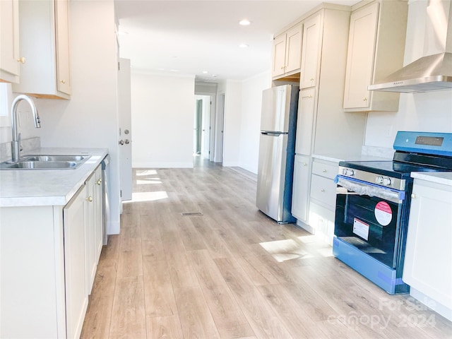 kitchen featuring sink, stainless steel appliances, wall chimney range hood, light hardwood / wood-style floors, and white cabinets