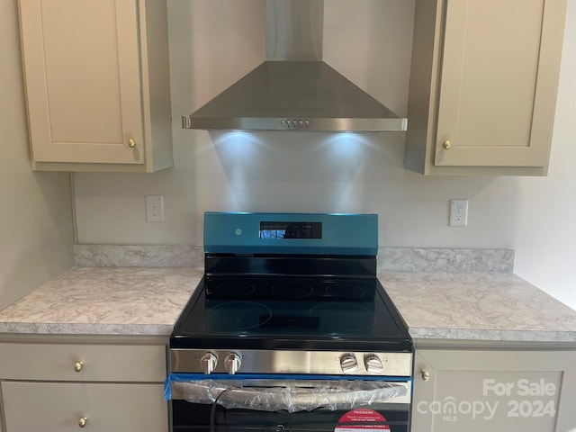 kitchen featuring gray cabinetry, wall chimney exhaust hood, and stainless steel range oven